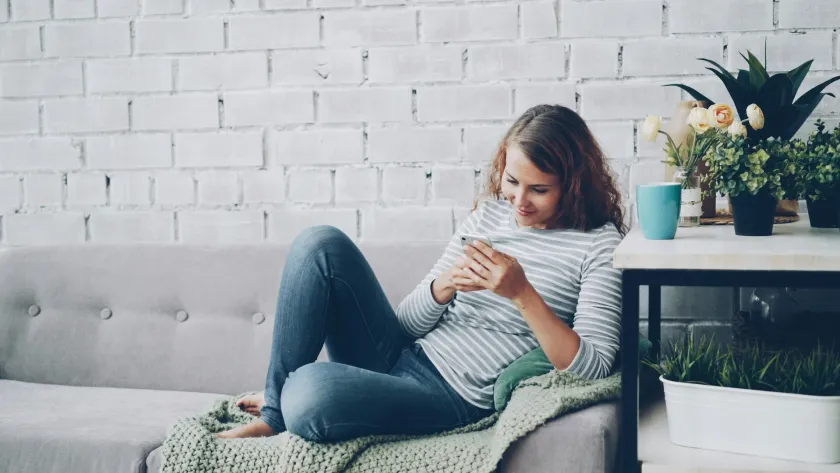 Mujer revisando su saldo y movimientos desde el teléfono, relajada en casa