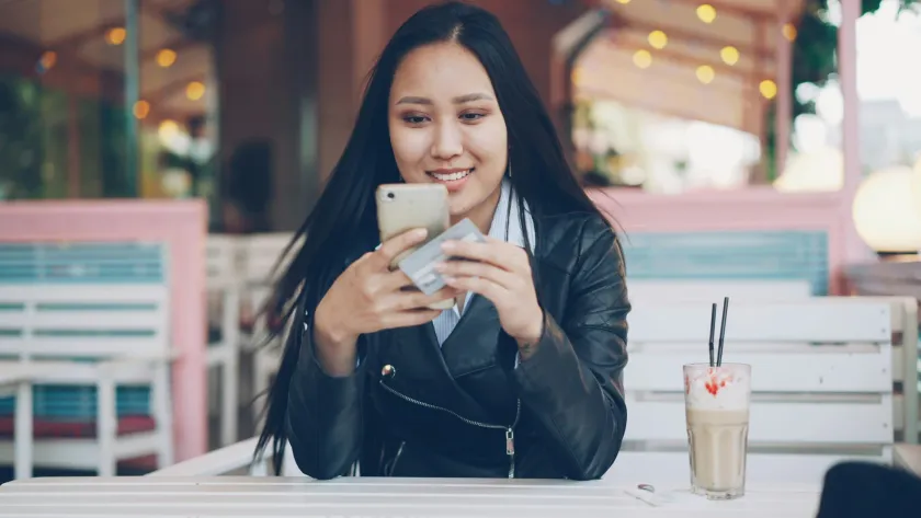 Mujer realizando un pago desde su teléfono con tarjeta en mano