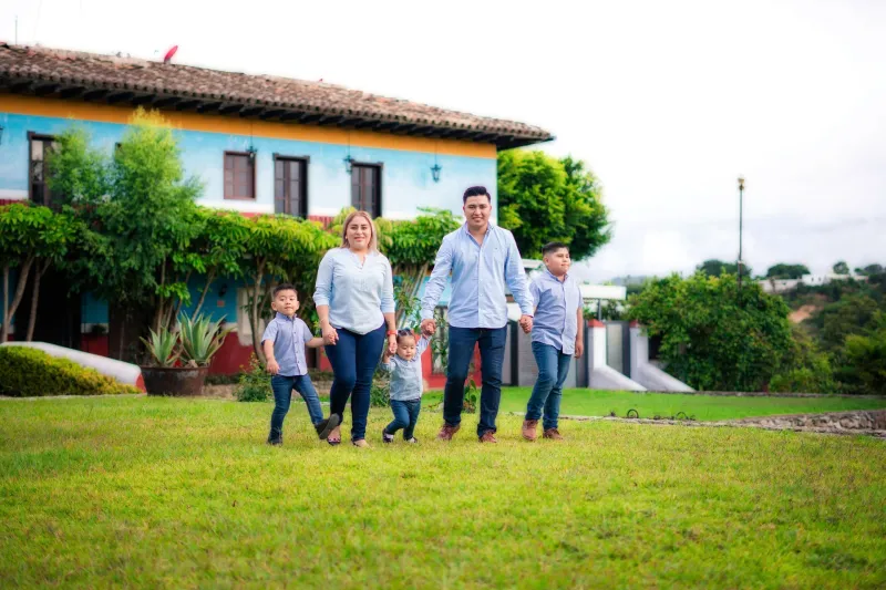 Familia caminando de la mano frente a su casa, representando la visión de progreso y futuro de los socios de COOPCASA